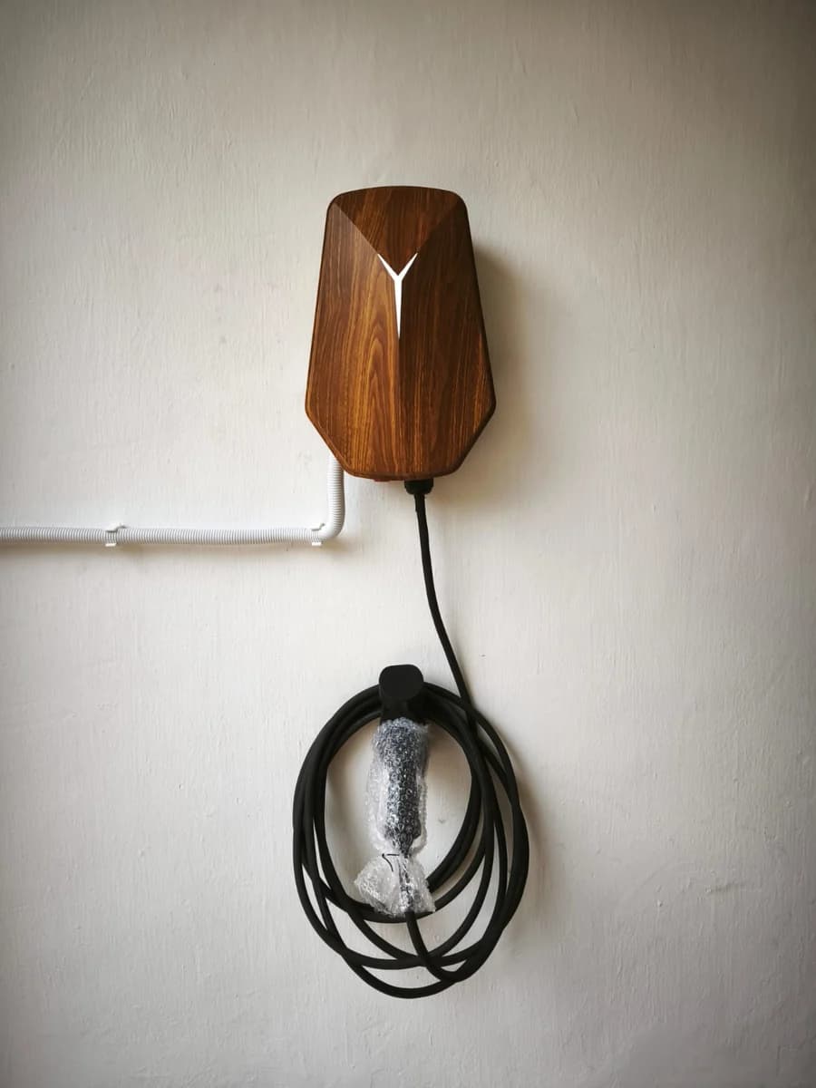 A wood-grain HiCi charger with white conduit entering from the side and the cable coiled beneath.