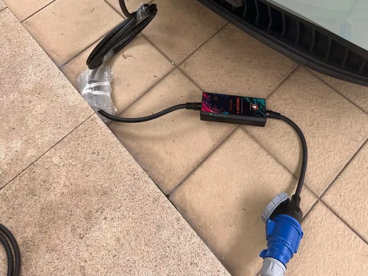 A portable EV charging set on the ground at a Singapore home, its in-line control box and blue industrial plug beside the car