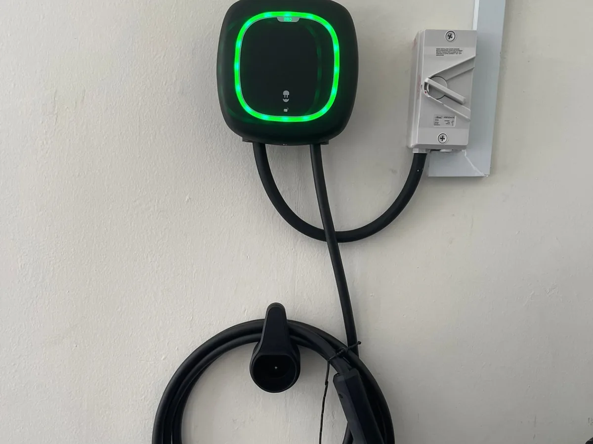 A compact wall-mounted EV charger with a green status ring, its isolator switch and holstered Type 2 connector at a Singapore home