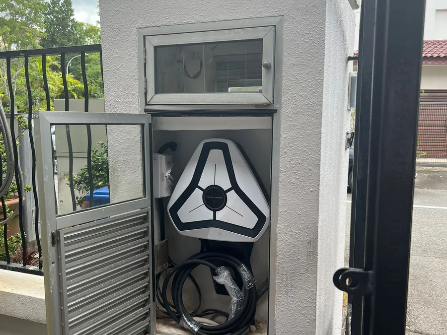 A white three-spoke charger mounted inside a rendered enclosure with a service hatch above and a metal gate in front.