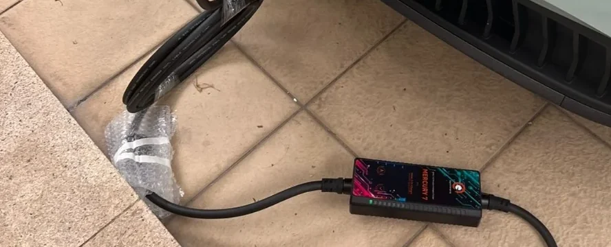 A Mercury 7 portable charging unit resting on a tiled driveway, its cable running up to the car alongside and the connector's protective wrap set down next to it.