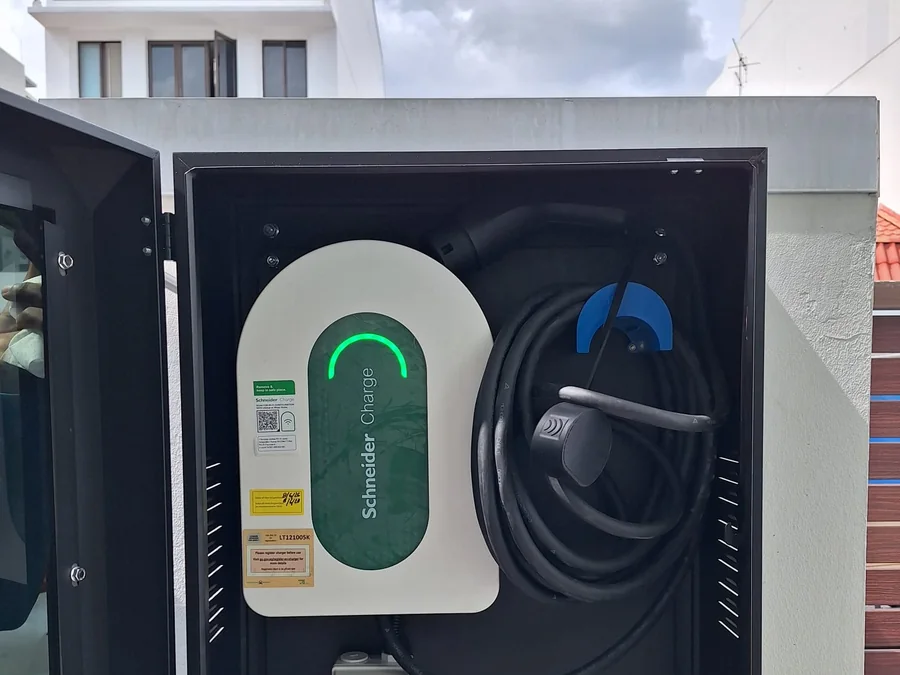 A white Schneider Charge unit inside an open lockable enclosure, its blue-tipped connector stowed alongside and commissioning documents in the cabinet.