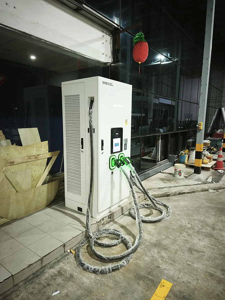 A floor-standing white DC charging cabinet seen at an angle, its ventilated side and two green-lit connector holsters visible, its cables still in factory wrapping and coiled on the concrete.